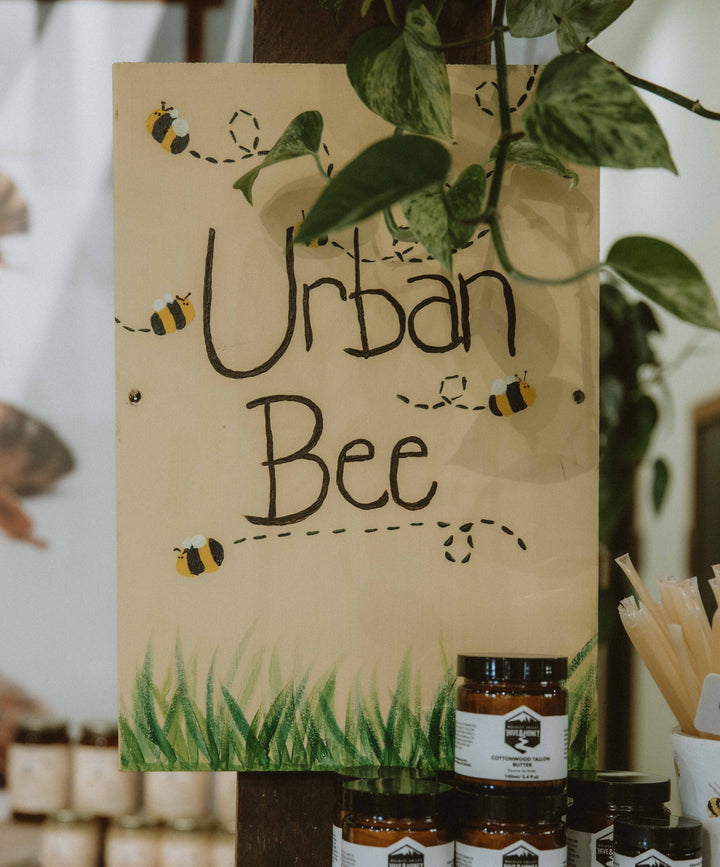 Wooden sign with 'Urban Bee' branding next to jars on a wooden shelf.
